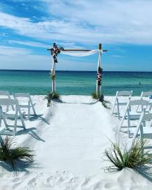 2 pole bamboo arbor with white sheer fabric and flowers and 30 white padded chairs on Panama City Beach, FL