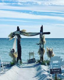 Driftwood Arbor white sheer fabric, pompous grass, sand ceremony table and 50 white padded chairs
